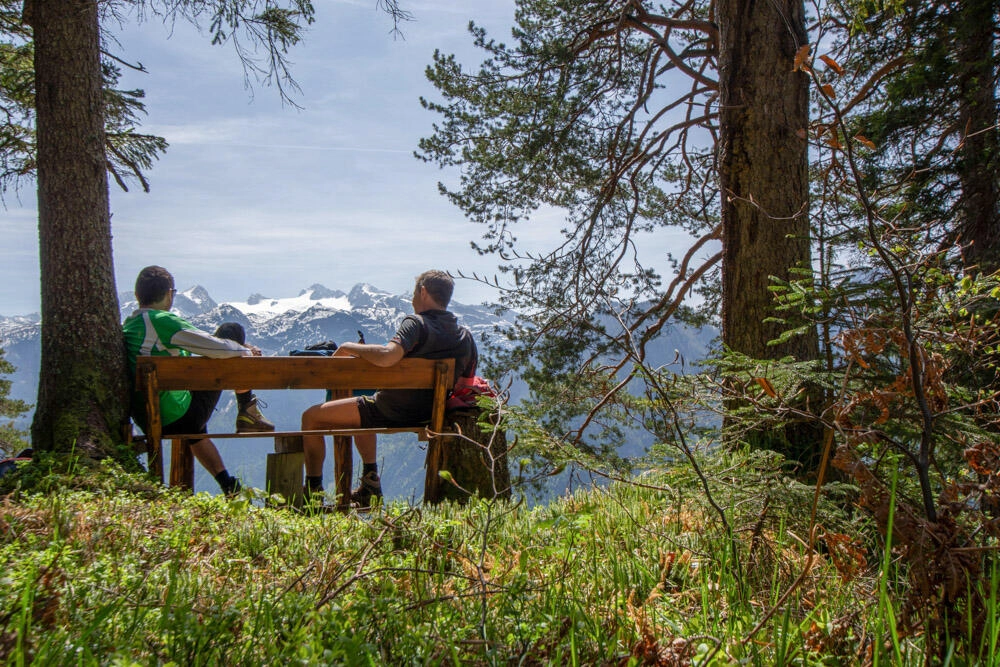 Zwei Wanderer die sich gerade auf einer Holzbank auf einem Berg ausruhen und die Aussicht geniesen.