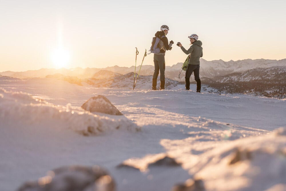 Skitour-Sonnenaufgang-Rast-Foto-OOE-Tourismus-Dachstein-Salzkammergut-Michael-Groessinger Eine Frau und ein Mann stehen bei Sonnenaufgang auf der Hochfläche des Dachsteingebietes.