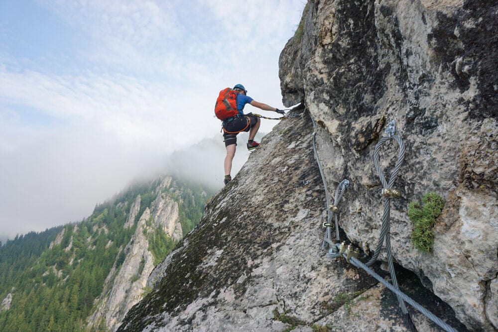 Stunning shot of a young man climbing up a cliff on a cold and foggy day Ein Mann der gerade eine Felswand hochklettert